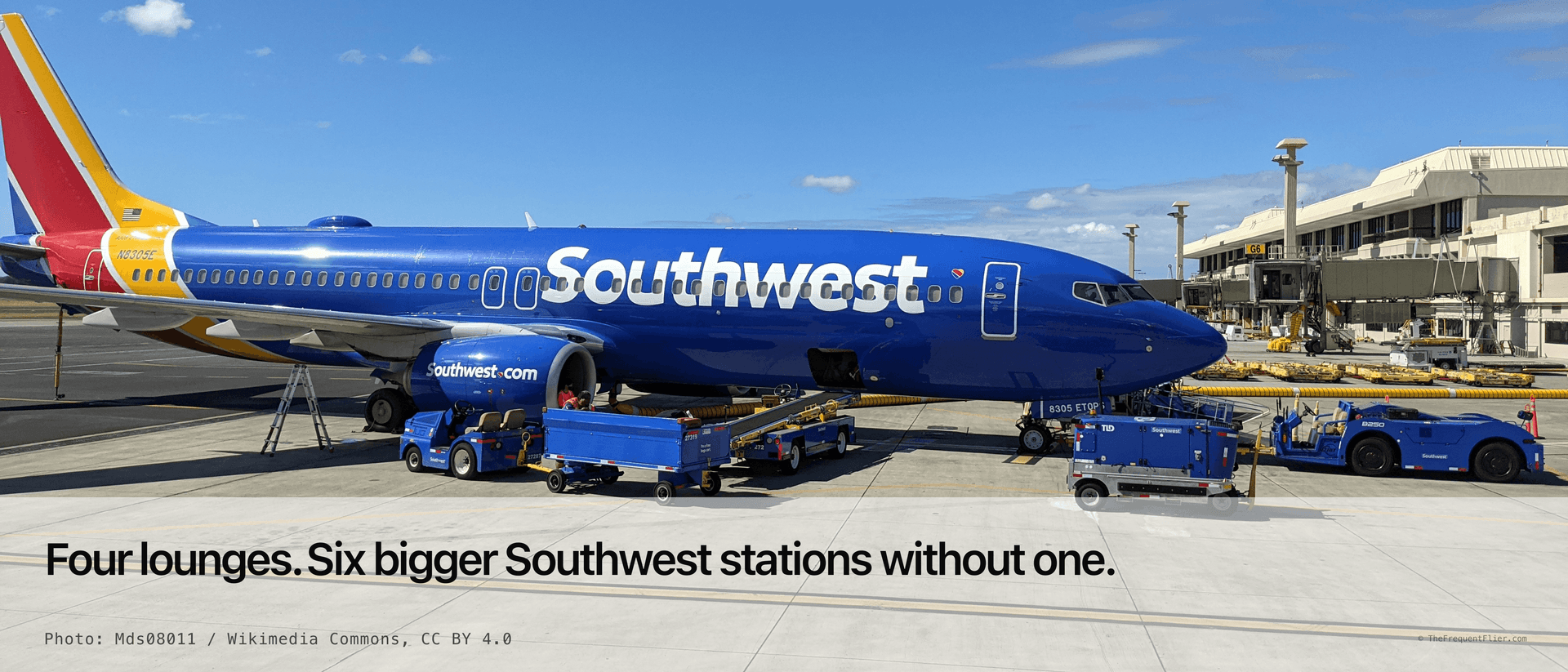 A Southwest Airlines Boeing 737 in the blue Heart livery parked at a gate at Honolulu, baggage carts and a pushback tug on the apron in front of it and the terminal jet bridge behind.